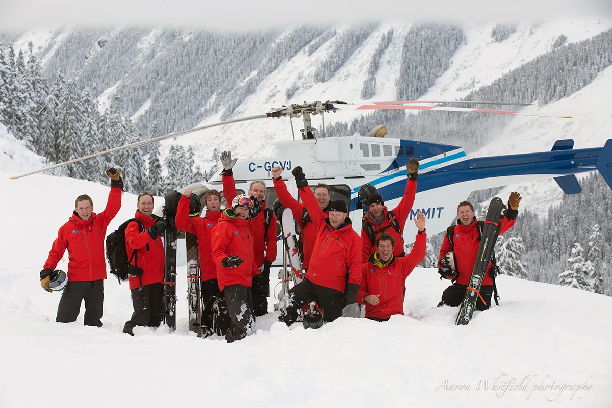 Northern Escape heli-ski guide team raising their arms beside the helicopter in the Skeena Mountains near Terrace, BC.