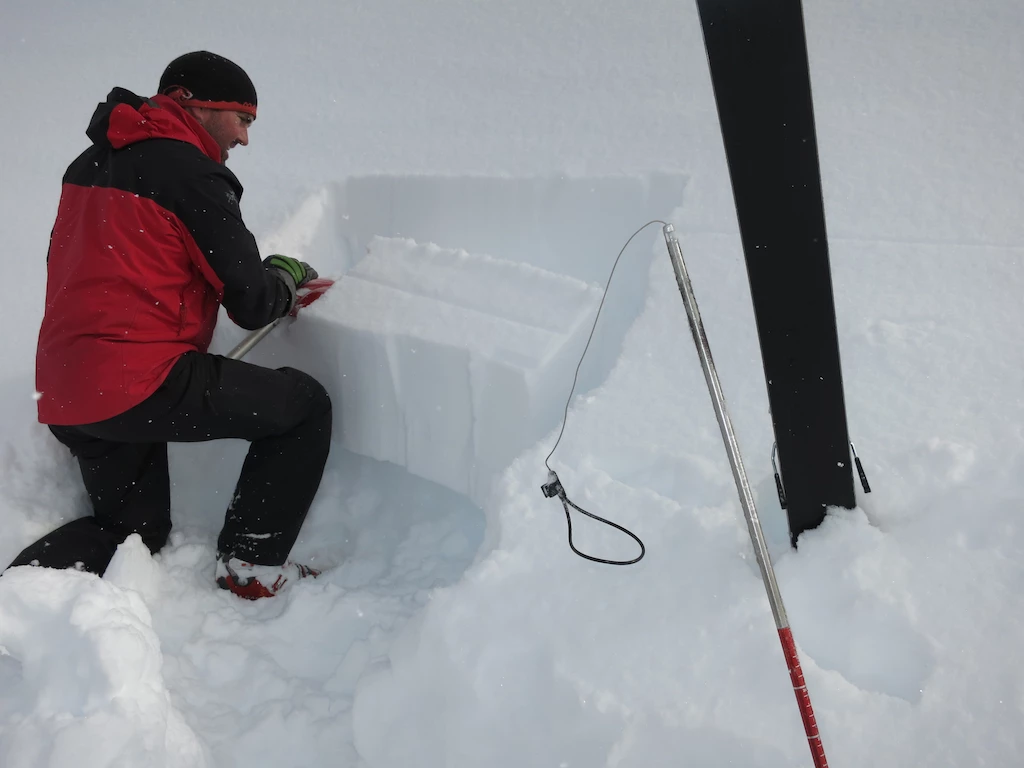 Northern Escape snow safety team member digging a snow pit to check snowpack layers in the Skeena Mountains.